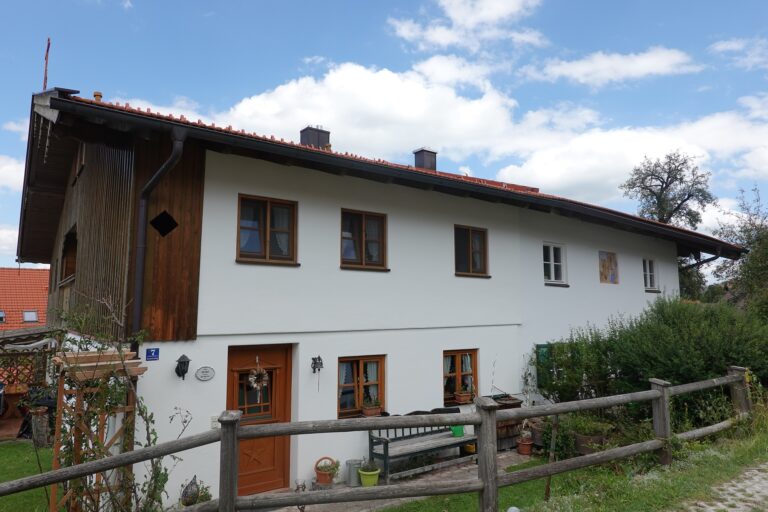 Älteres Wohnhaus mit weißer Fassade, Holzfenstern und Holzzaun unter Wolkenhimmel