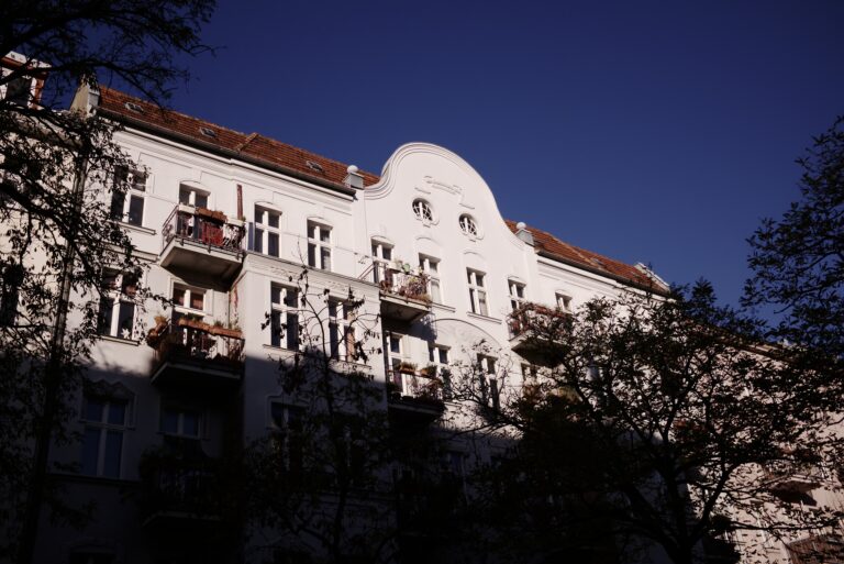 Weiße Altbaufassade eines Mehrfamilienhauses mit Balkonen und Ziergiebel im Abendlicht